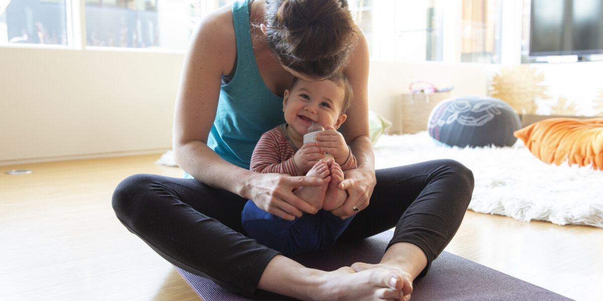 Mother on yoga mat holding cute, happy baby