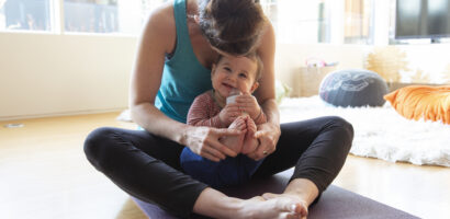 Mother on yoga mat holding cute, happy baby